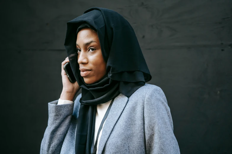 a woman in a gray jacket and black scarf is talking on a cellphone