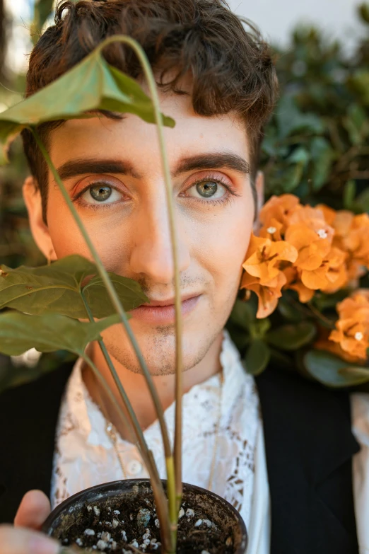 man with blue eyes holding up potted plant and leaves