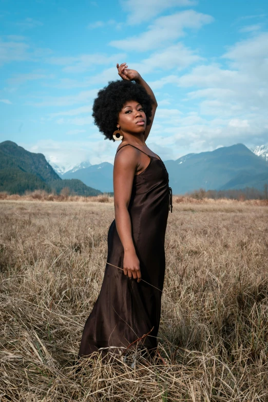 a woman in a dress stands in an empty grass field