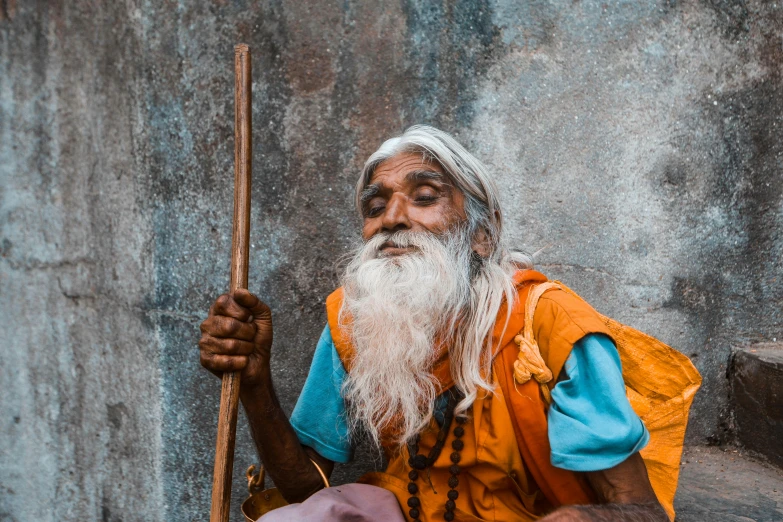 a bearded man sitting down and holding a pole