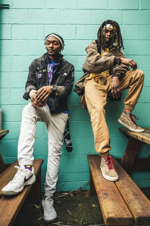 two men sitting against a blue wall with their feet crossed