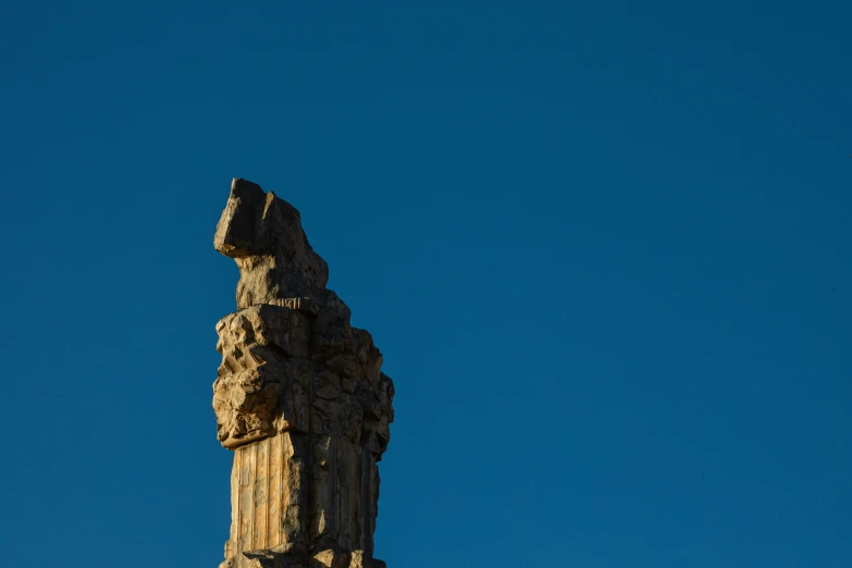 a tall rock structure with a small bird flying in the sky