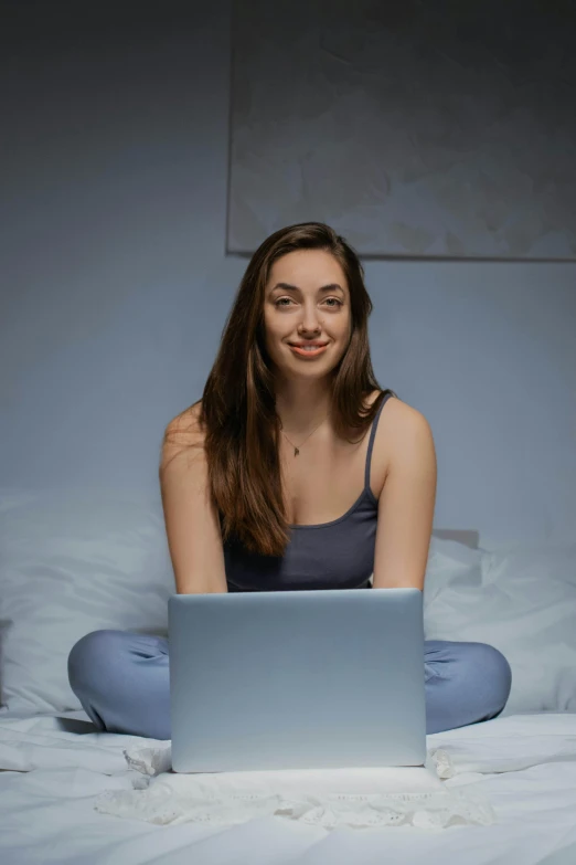 a woman smiles while using her laptop on the bed