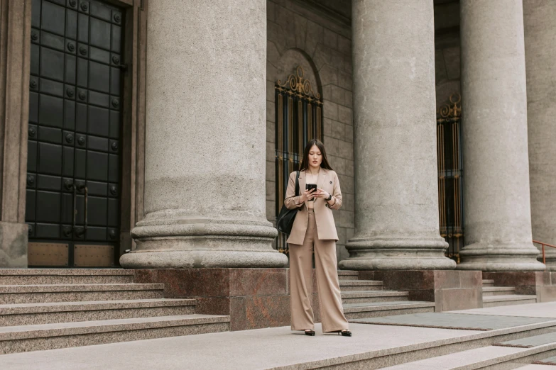 a woman in a long suit stands on the steps with her phone