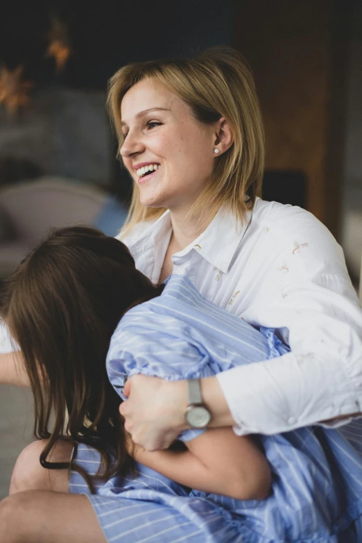 the woman in the blue dress smiles while holding a girl in the blue  pajamas