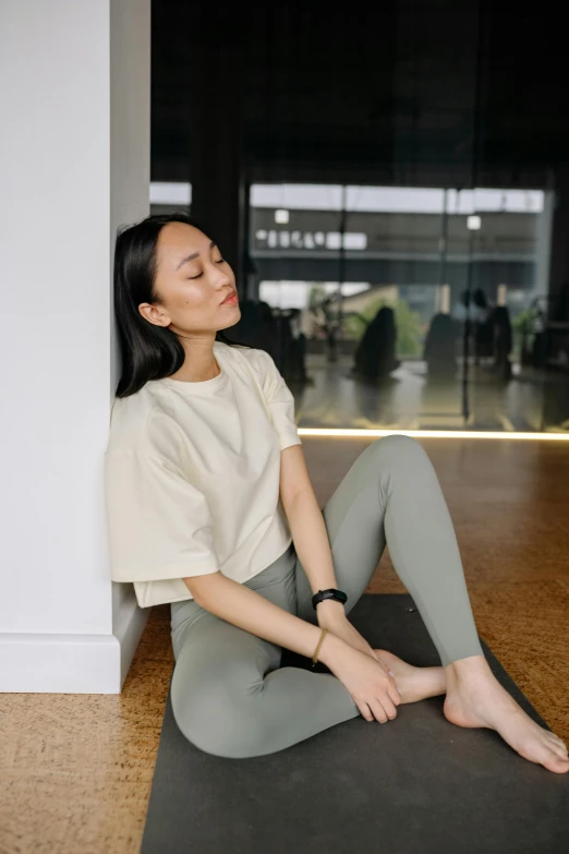 a woman sitting in a yoga position wearing a white top and gray pants