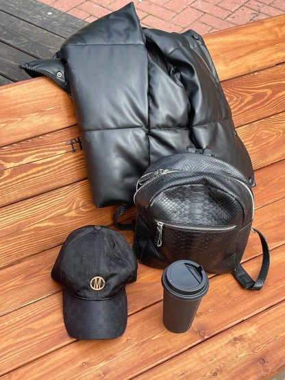 a leather purse, coffee mug and a hat sit on a wooden bench
