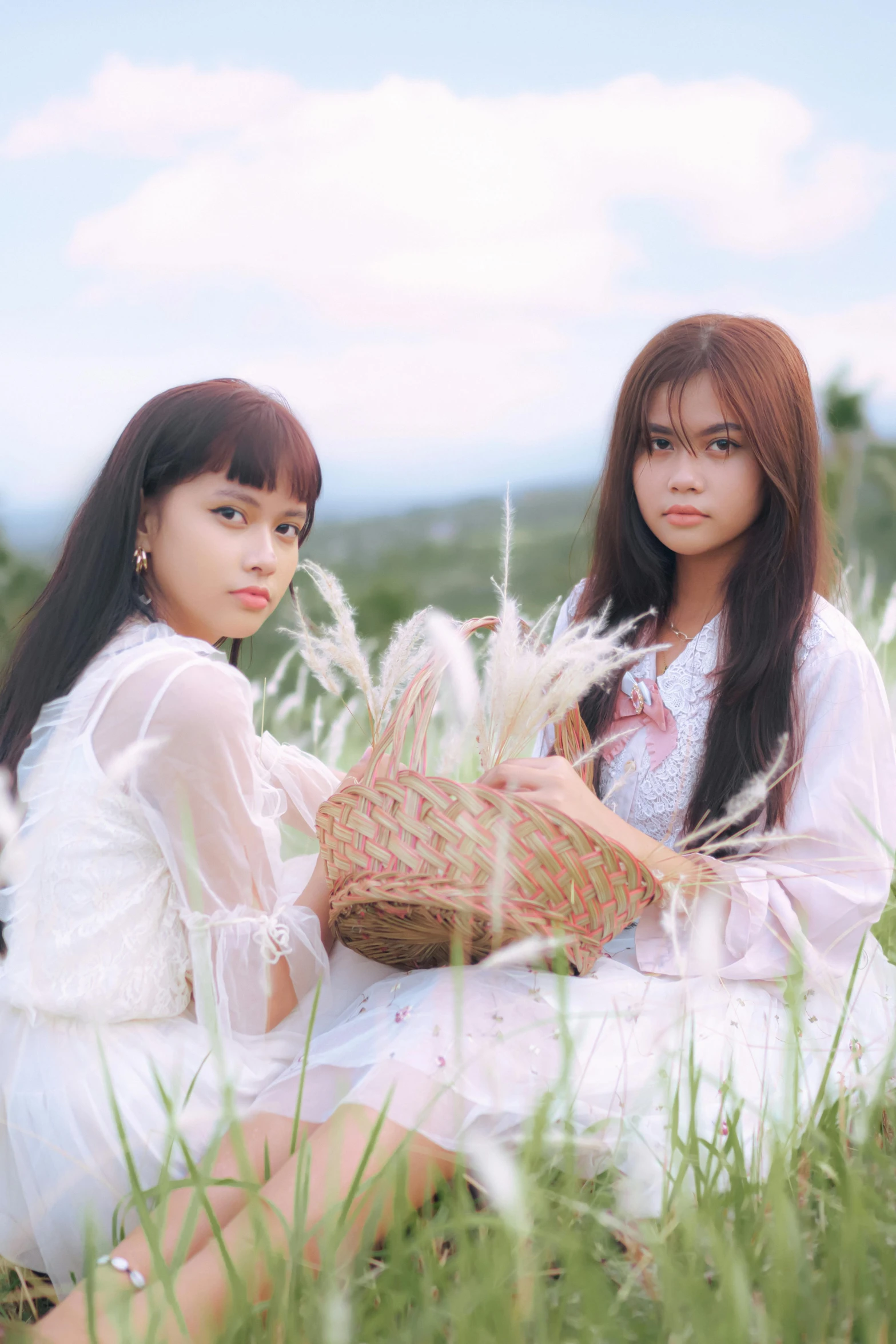 two asian girls sitting on the grass one is holding a basket