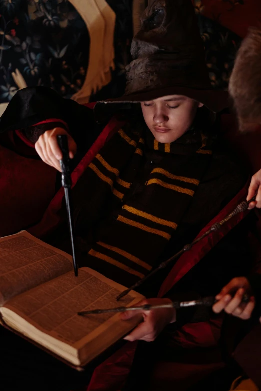 a young child wearing a harry potter hat, reading a book