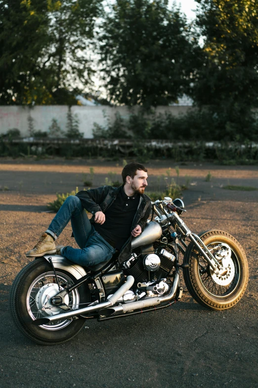 a man wearing jeans and an black t - shirt sits on a motorcycle