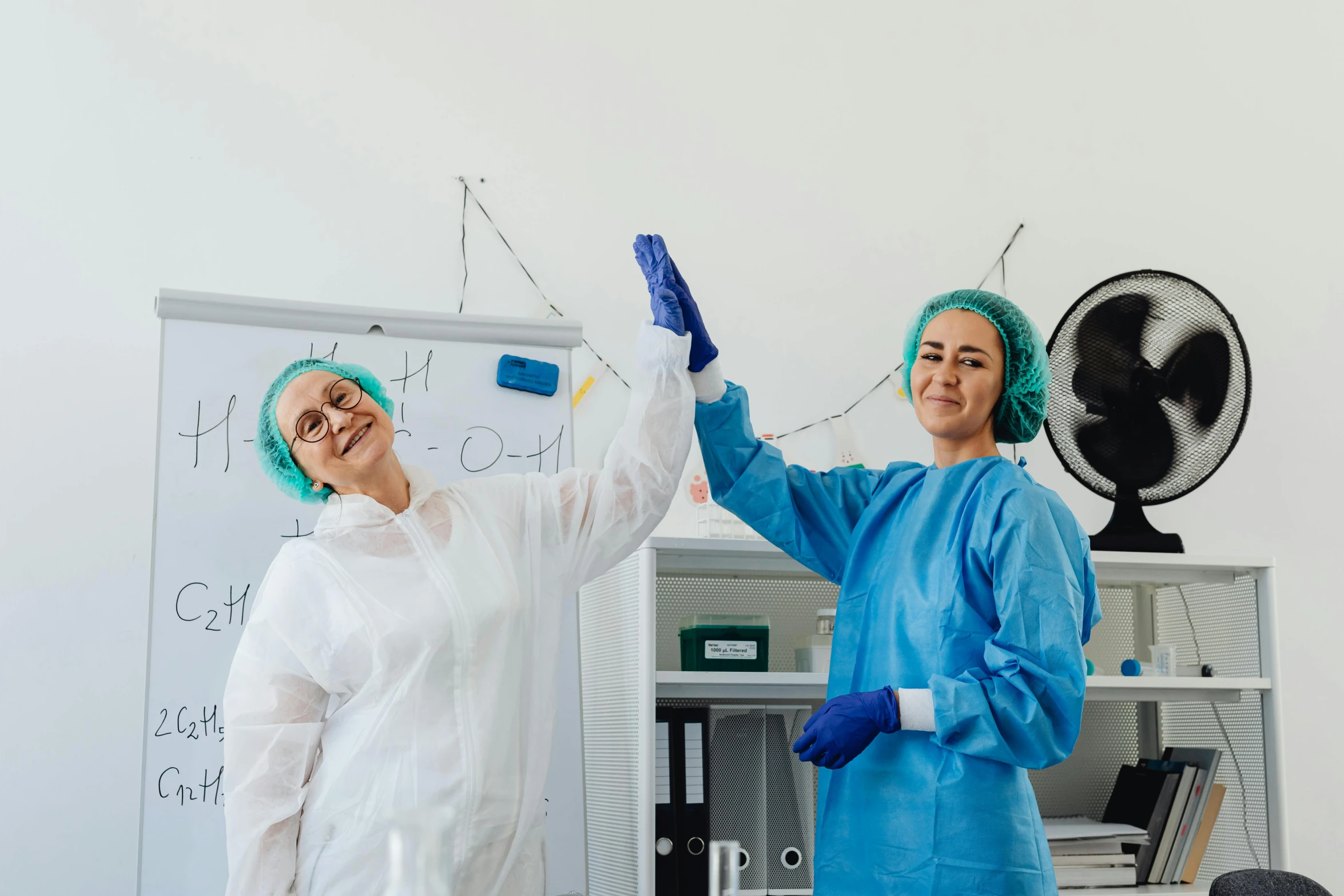 two women in scrub coats and latex gloves are doing soing