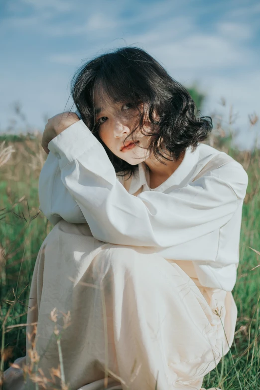 the woman in the white dress is sitting in a field of grass