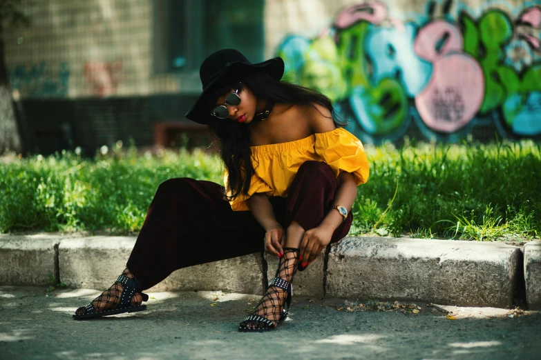 a woman with long black hair in a yellow top sitting on a curb