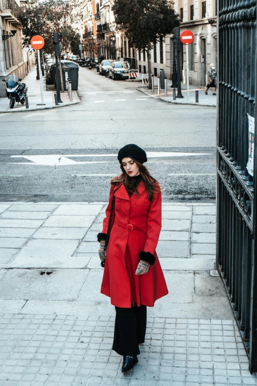 a woman in red coat standing on sidewalk next to metal gate