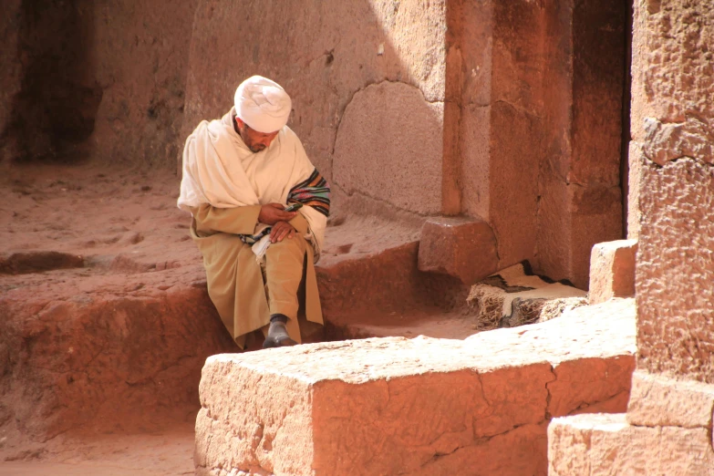 a man in an ivory colored outfit sitting on some bricks