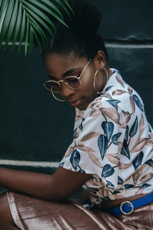 a girl wearing glasses sitting down on the ground next to plants