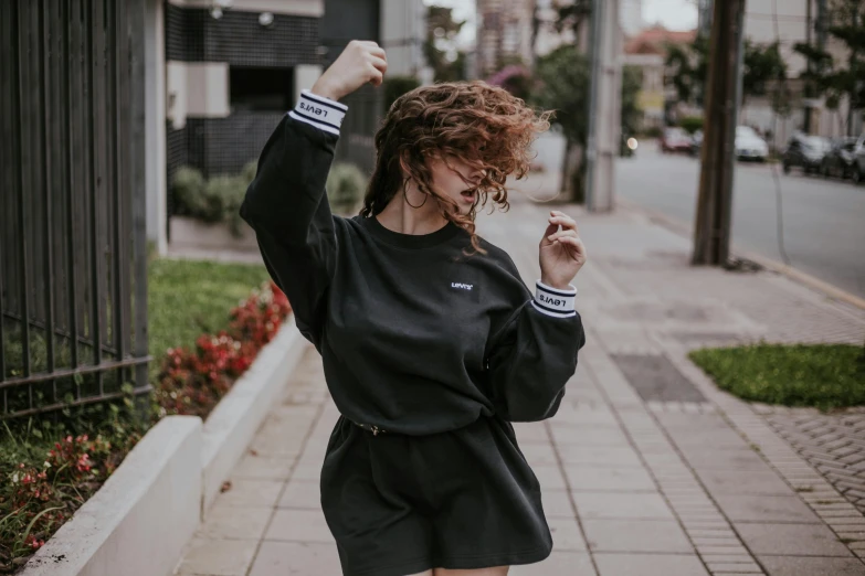 a girl in a sweatshirt and shorts poses while holding her hand up