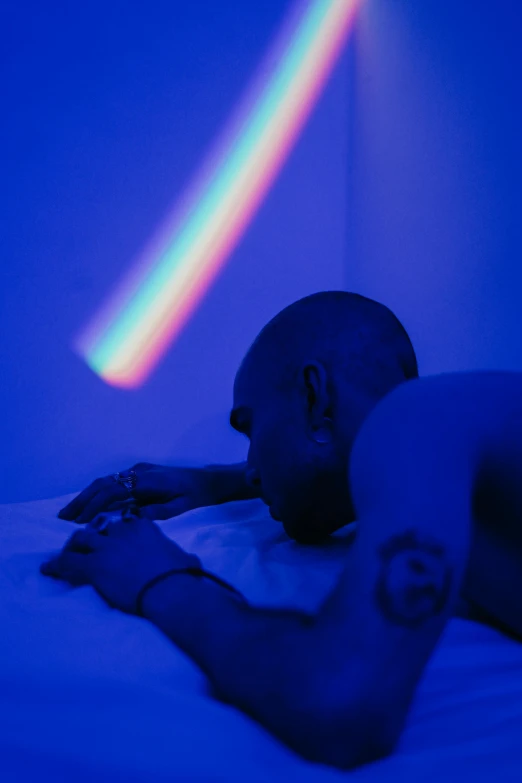 man in white shirt laying on bed in room with purple light