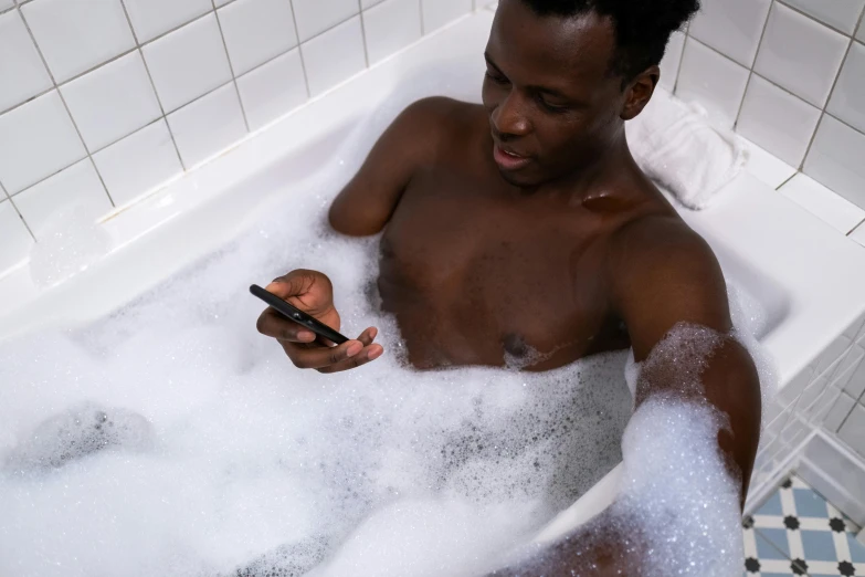 a black man takes a bath with soap and a cellphone