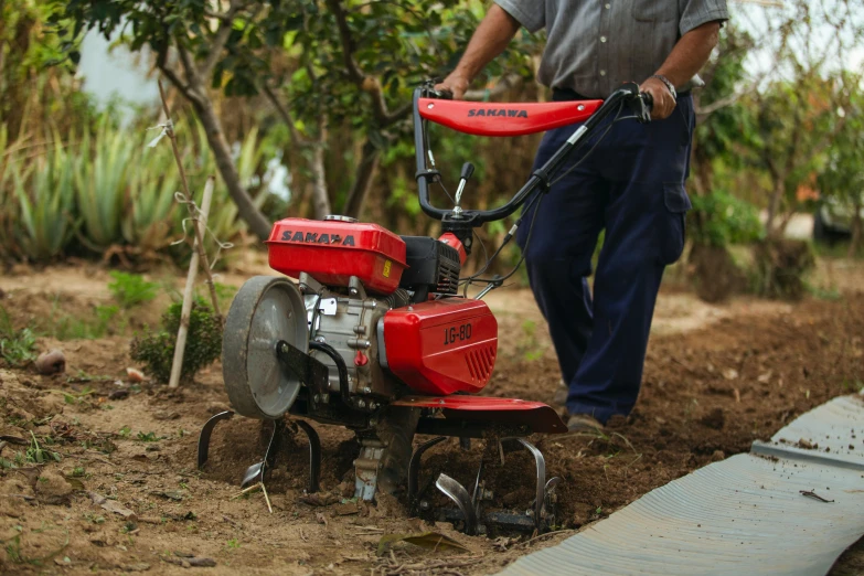a man walks behind a small tractor in the dirt