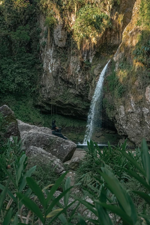 the waterfall has a man in it sitting on a rock