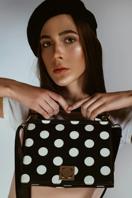 a woman wearing a white top is holding a black and white polka dot bag