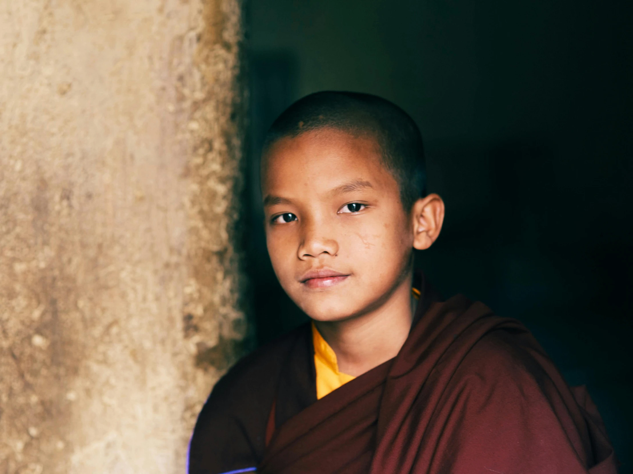 a young monk stands by a tree next to a wall