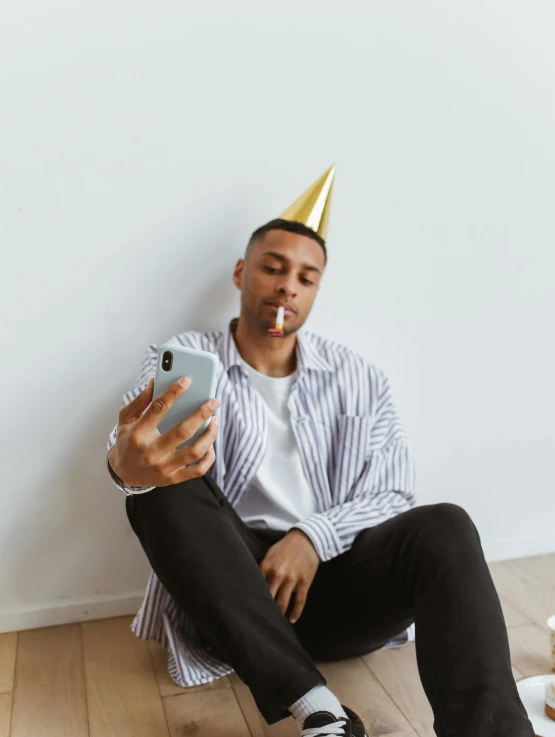 a man with a party hat sitting down while looking at his cell phone