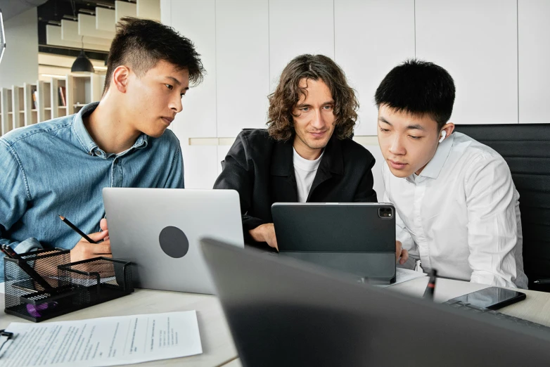 three men looking at computer screens on desk