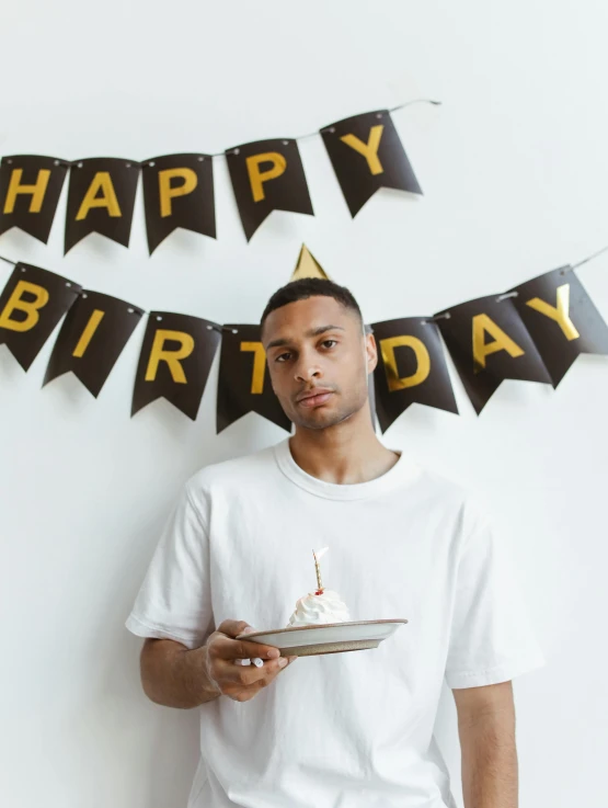 a man holding a piece of cake while standing in front of a birthday sign