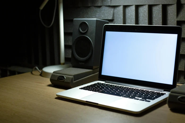 an open laptop computer on a desk with speakers behind it