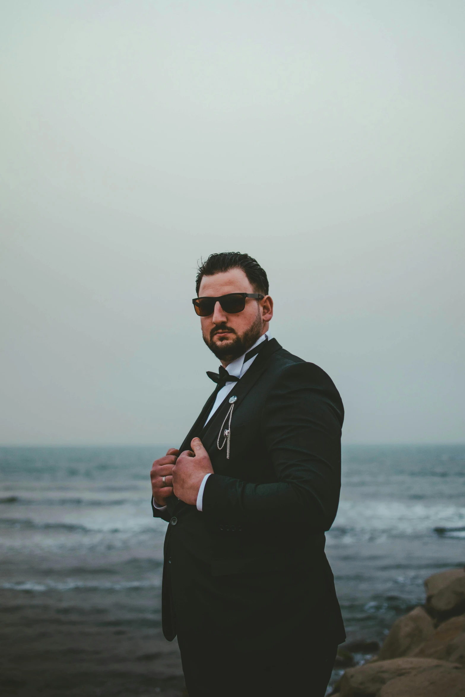 a man standing by the water in a suit and sunglasses