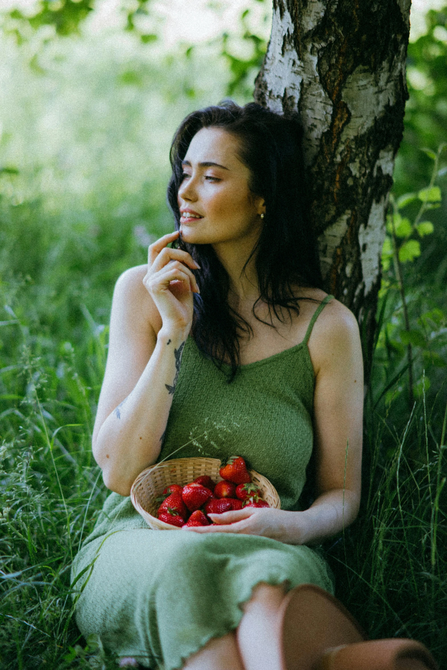 a woman in a dress eating some fruit in front of a tree