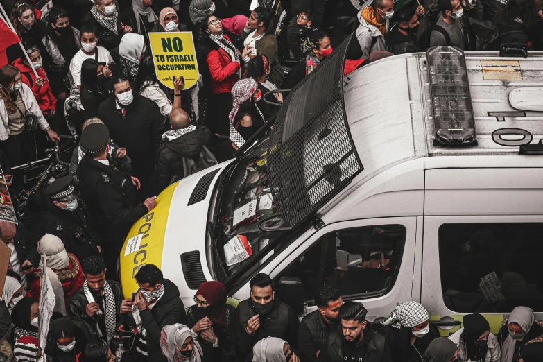 large crowd of people gather with signs and a van