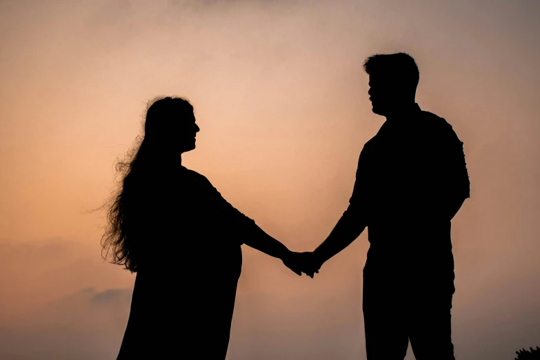 silhouette of two people holding hands against an orange sky