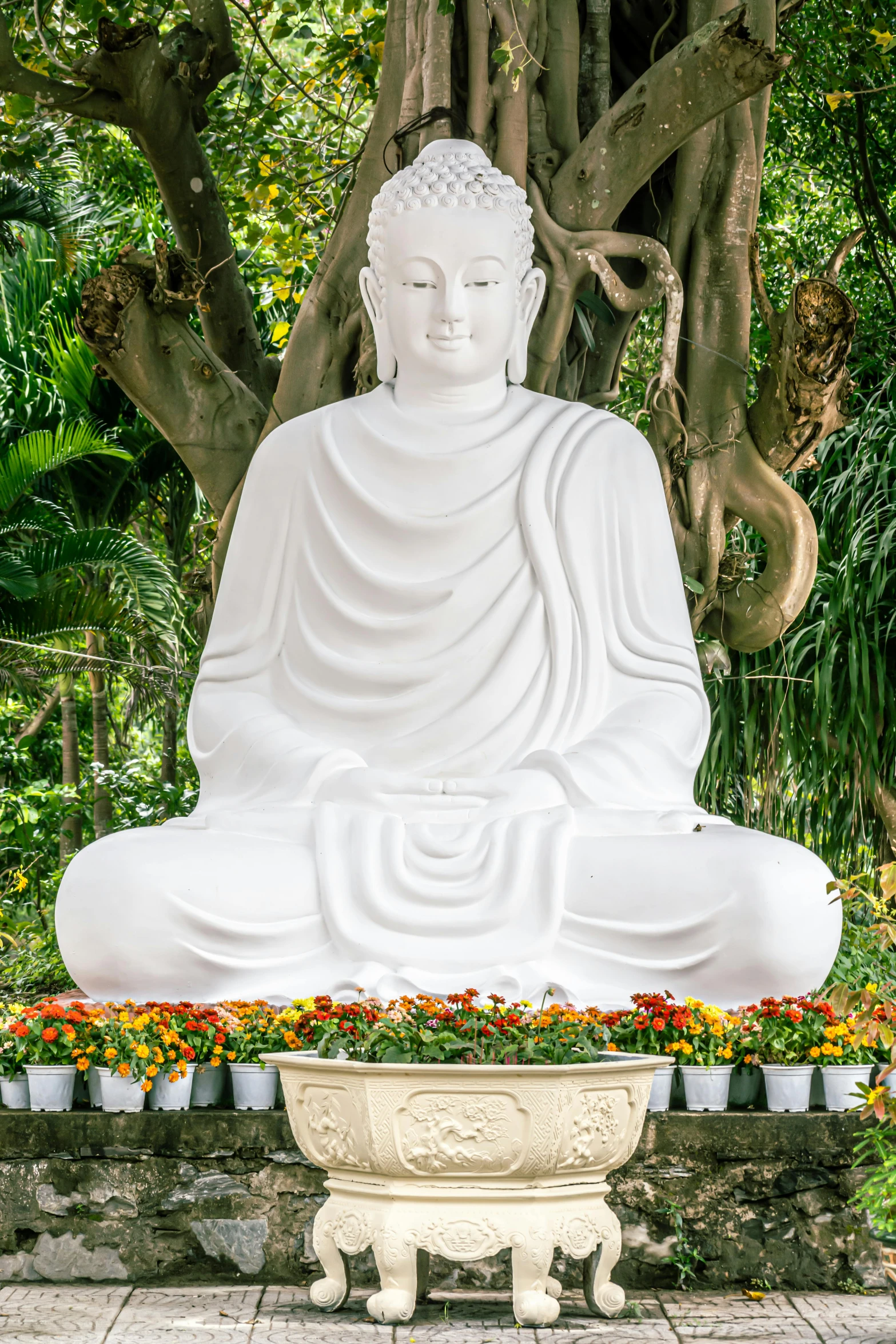 a large white buddha statue sits surrounded by plants