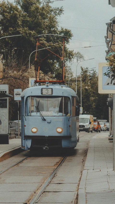 a blue trolley is coming down the tracks on the street