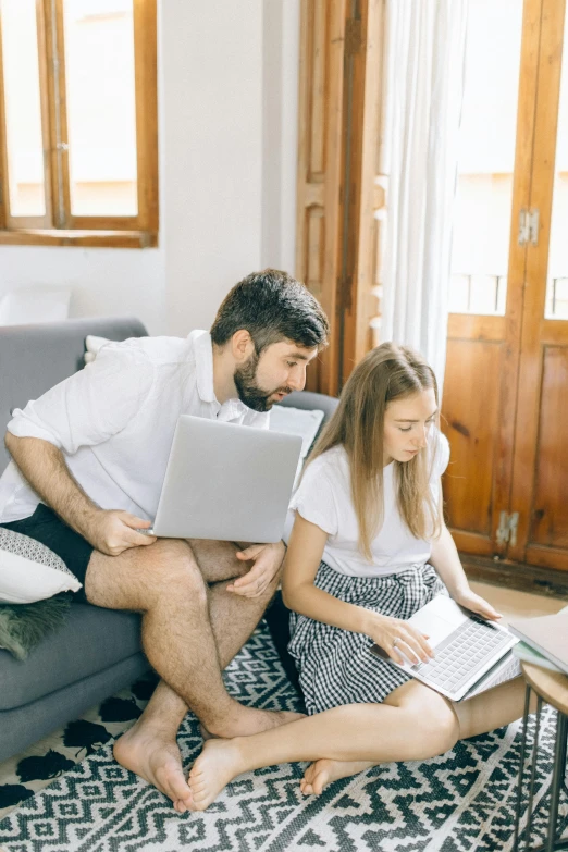 two people sitting on a couch using laptops