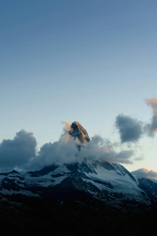 a snow covered mountain with clouds around it