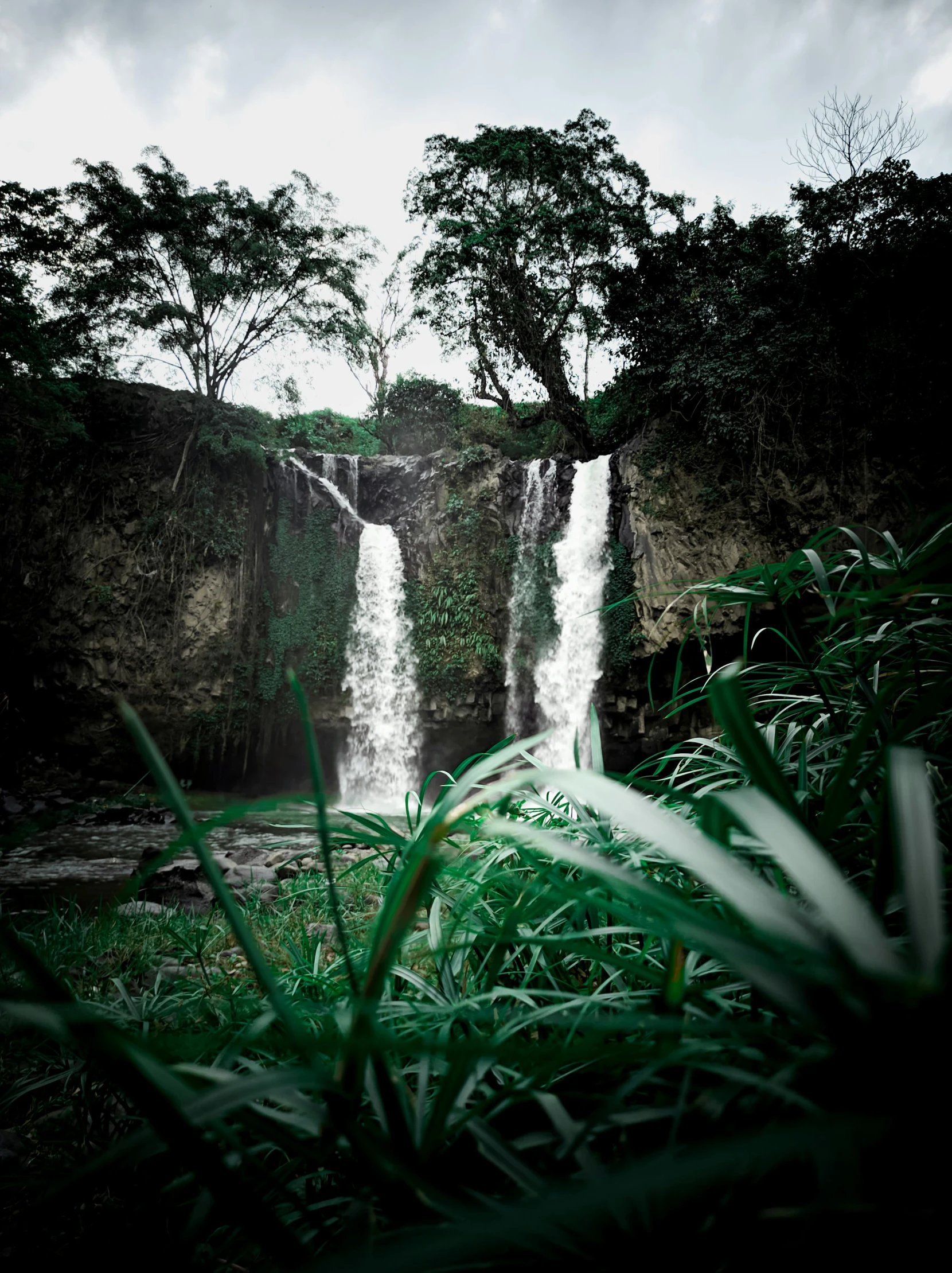 large waterfall next to lush green jungle under a cloudy sky