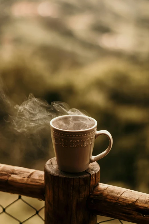steaming coffee cup on fence rails in the mountains