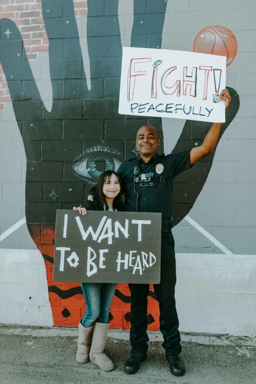 a couple poses together holding signs in front of a large mural