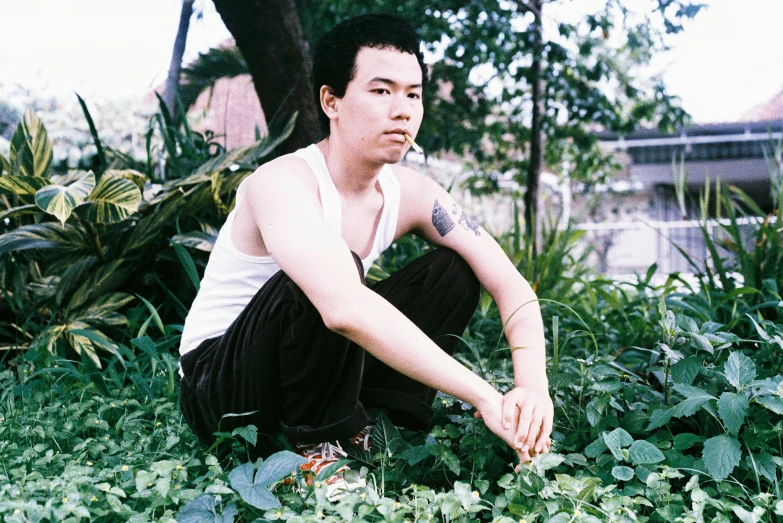 a man squatting in a weedy area next to plants