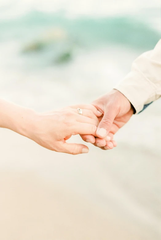 a couple holding hands on a beach with waves in the background