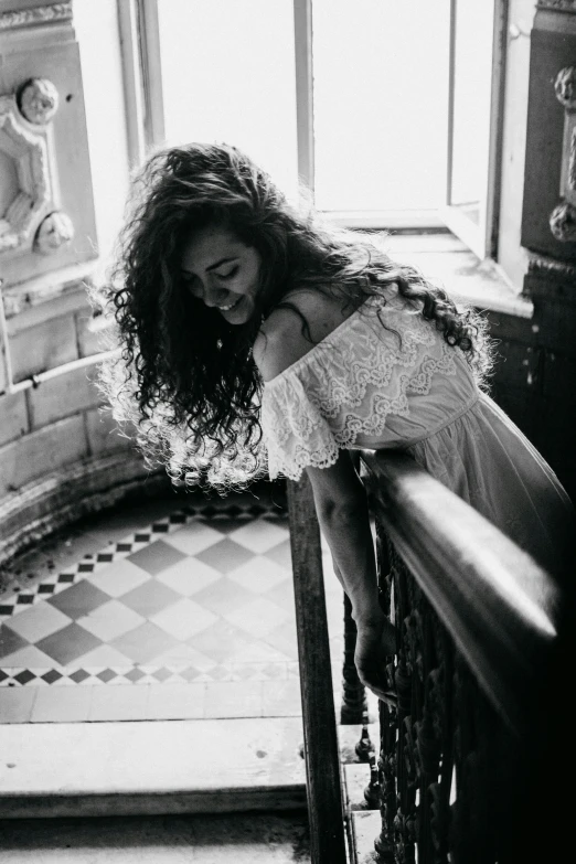 girl leaning over railing of old staircase looking down at floor