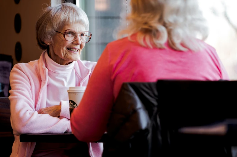 older woman at table drinking coffee and talking with younger lady