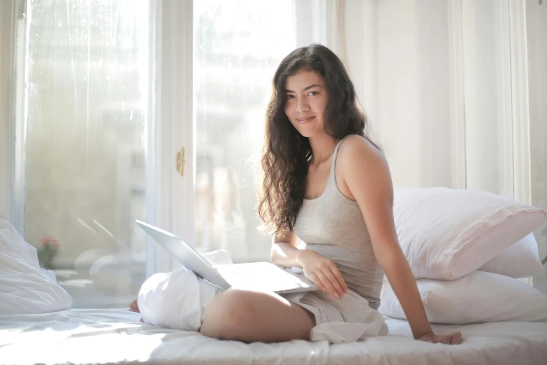 a beautiful young lady with long hair using a laptop on her bed