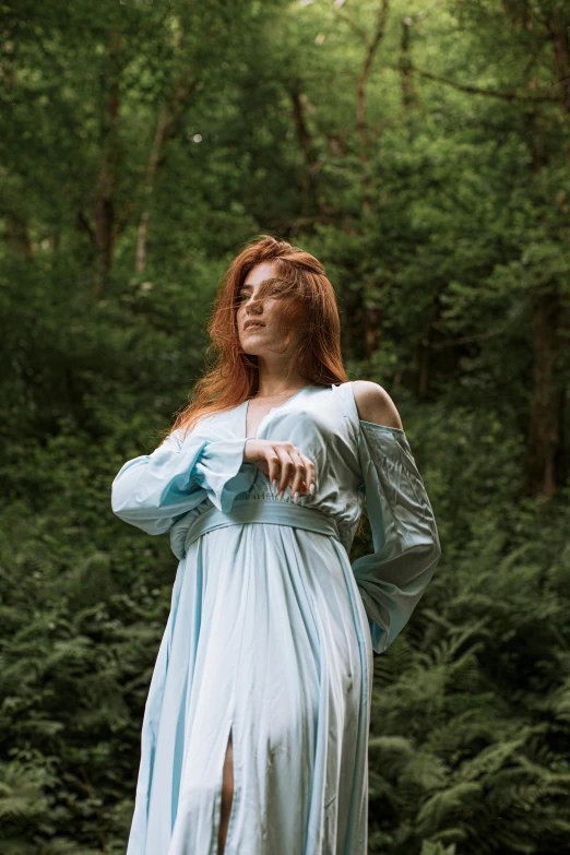 a woman in a blue dress standing next to the woods