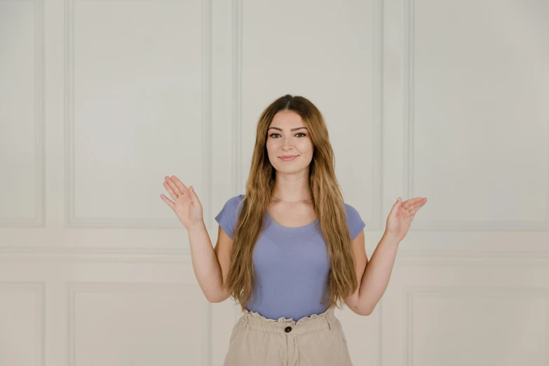 a girl standing in front of a white wall holding her hands up