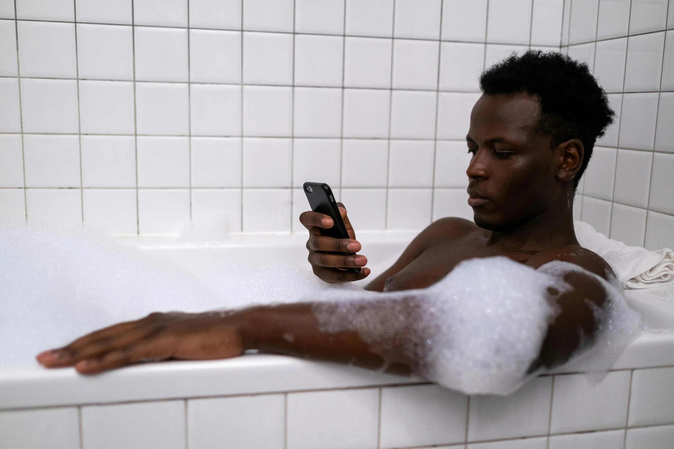 man using cell phone in bathtub, taking selfie with foam